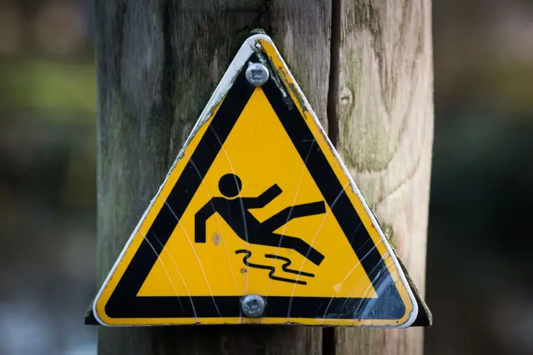 sign-slippery-wet-caution Yellow slip and fall warning sign mounted on a wooden pole outdoors