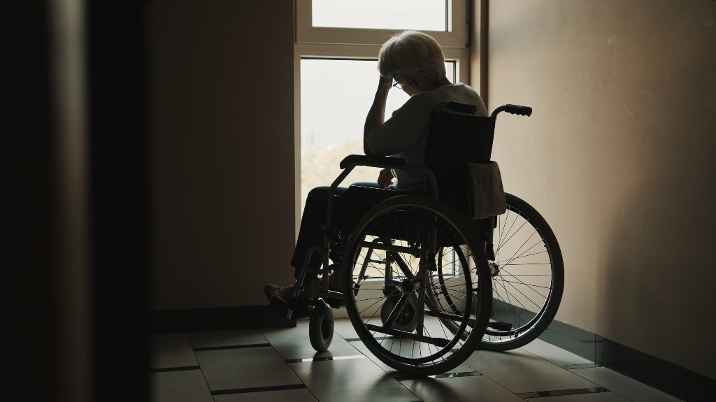 senior woman looking through the window of the nursing home_s Elderly Nursing Home Resident Sitting Alone In Wheelchair