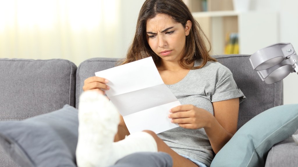 Woman With Injured Leg Reading Insurance Claim Denial Letter