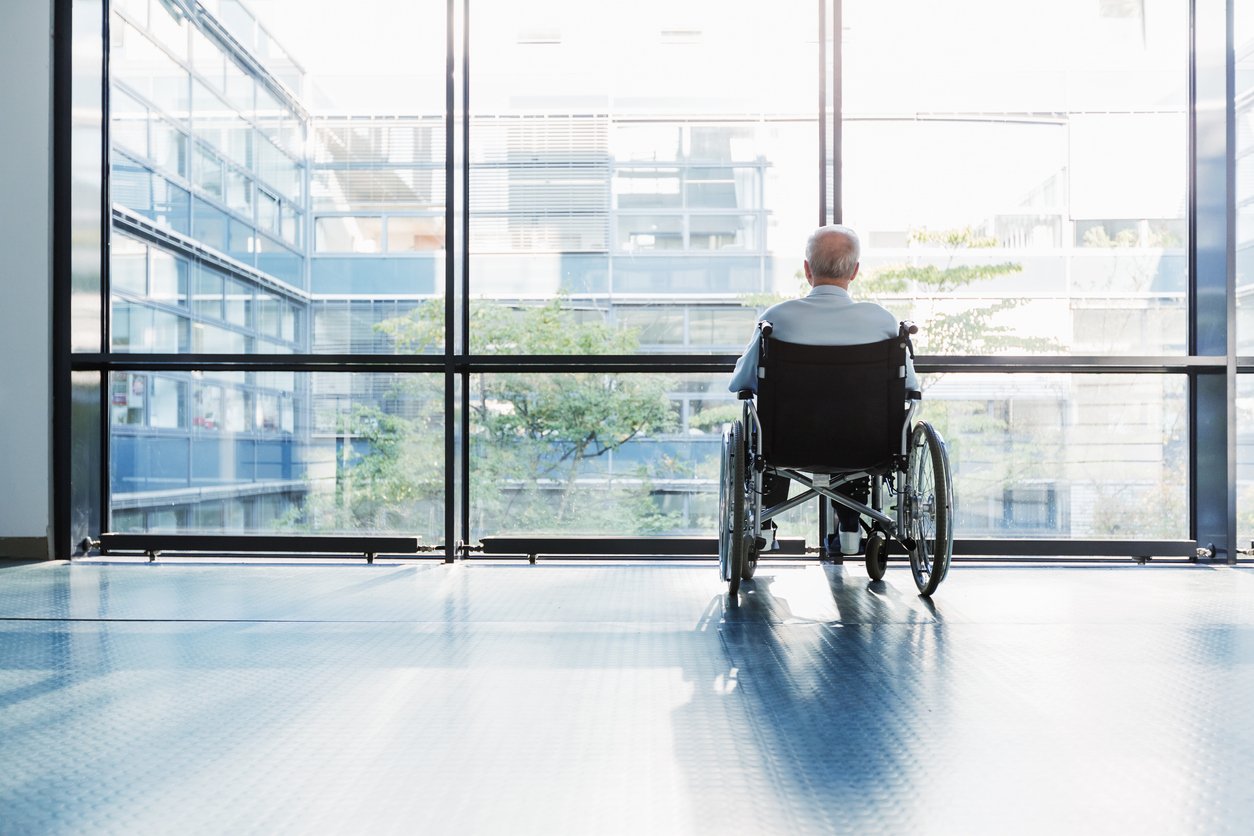 Elderly nursing home resident sitting alone in wheelchair near window representing isolation and signs of nursing home neglect.