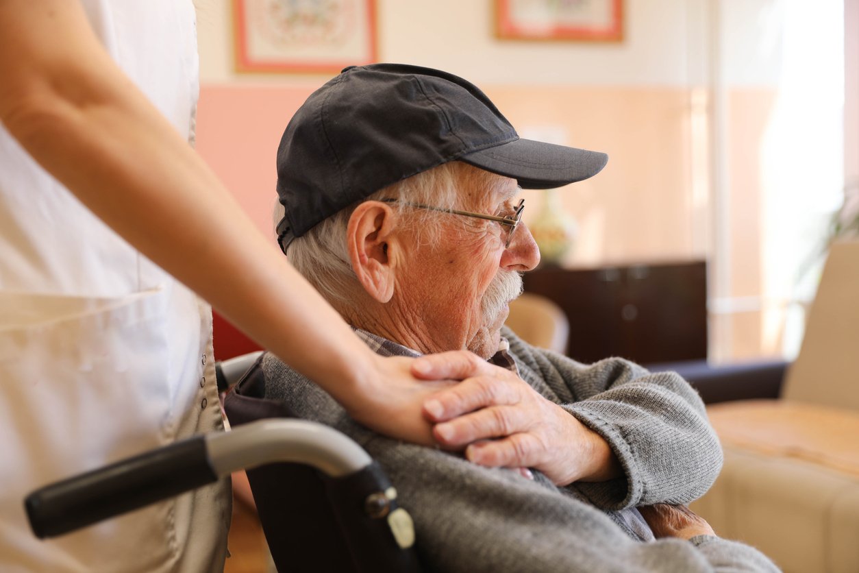 Caregiver supporting elderly man in wheelchair at nursing home facility to represent elder care and abuse prevention.
